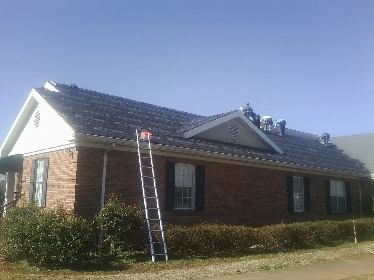 Crew tearing shingles off a brick ranch roof with a ladder set — Metal Roof Repair work by our crew in Collegeville