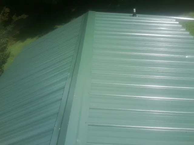 New green metal panels meeting at the ridge of a roof — Flat Roof Repair work by our crew in Collegeville